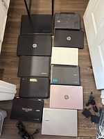 Top view of 11 laptops arranged on floor, various brands including HP, Lenovo, Acer, Samsung, some with visible wear and damage.