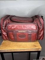Photo of a Rustic brand red leather camera bag, showing front and top zippered compartments on a wooden table.