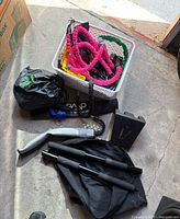 Photo showing multiple rolled elastic resistance bands with colorful sleeves, black adjustable straps, foam handles, and a door anchor all in a white basket and on the floor.