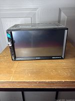 Front view of Jensen CMM7720 showing large touchscreen, volume knob, USB and auxiliary ports on side panel