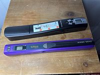 Top view showing two VuPoint Solutions Magic Wand digital scanners, black and purple, on wooden surface
