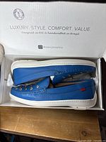 Pair of blue leather moccasin slip-on shoes in box with box lid visible showing brand text.