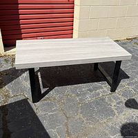 Rectangular coffee table with thick butcher block style top and black metal legs, photographed outdoors from an angle.