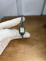 Photo of NY&C ladies quartz watch held with gloved hand showing square display and rhinestone accented black metallic band