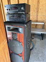 Photo of two Sony audio control units stacked on top of a large 4ft speaker showing front panels, controls, displays, and wood finish speaker front.