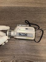 Silver Sony Mic'n Micro M-100mc microcassette recorder held in hand showing left side with labels and control buttons.