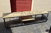 Rectangular TV stand with wood top and metal frame on paved surface outside storage units.
