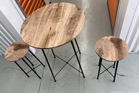 Overview of round wooden table and two matching stools from above on concrete floor in storage area.