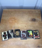 Front view of six Durolite refillable windproof lighters laid out horizontally on wooden surface, each with various printed designs.