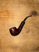 Wooden vintage tobacco pipe lying on wooden surface, showing curved bowl and black stem.