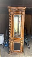 Full view of the tall wooden cabinet showing the glass door, ornate top edge, and twisted column on the side.
