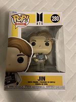 Front view of unopened box showing Funko Pop Rocks BTS Jin #280 vinyl bobble head inside with clear window display.