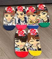 Photo shows six pairs of BTS character socks laid out on a floor, each featuring a colorful cartoon representation of a BTS member's face, with names and color-coded toes and heels, new with packaging.