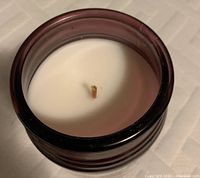 Close-up photo of the Cinnamon Stick candle showing white wax surface and wick in dark glass jar.