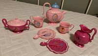 Photo showing all components of the pink Disney princess plastic tea set for children on a mattress surface.