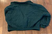 Back view of the green quilted fall jacket laid flat on a wooden floor, showing the elasticized waistband and sleeves.