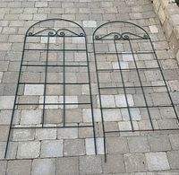 Two green metal garden trellises laid flat on stone patio, showing full length and decorative top detail.