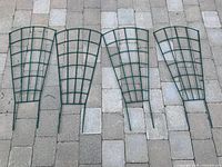 Four green metal garden trellises laid on a paved surface, showing size and shape as a group.