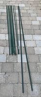 Multiple green plastic garden stakes of various lengths laid out on a paved surface, arranged side by side to show size difference.