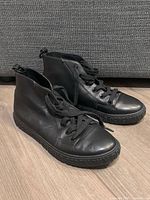 Side view of black high top shoes showing leather upper, laces, and the general shape and condition of the shoes.