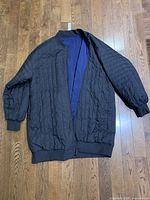 Black side of the jacket displayed flat, showing quilted nylon pattern and ribbed cuffs, collar, and hem.