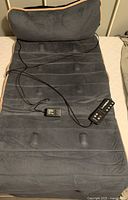 Dark gray massage pad laid out flat with an attached inflated pillow at the top. Includes the wired remote and power cord placed on the pad.