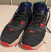 Front view of the pair of men's Nike shoes showing textured black upper with red accents, blue collar and green inner lining