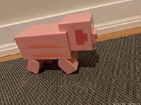 Side view of a pink LEGO Minecraft Piggy figure standing on carpeted floor, showing blocky legs and side body details.