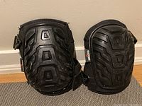 Pair of black knee pads with molded hard plastic protective caps, showing wear marks and signs of heavy use. Both knee pads have NoCRY brand tags attached.