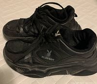 Side view of both black Playboy running shoes showing logo, lace-up design, and sole construction.