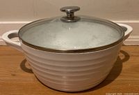 White ceramic Dutch oven with ribbed design and glass lid, shown closed on wooden surface