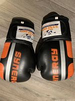 Pair of black and orange boxing gloves labeled 'SYNERGY' showing front and logo details