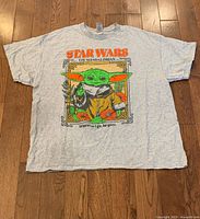 Light grey T-shirt featuring Baby Yoda (Grogu) from The Mandalorian with colorful graphic design and text.