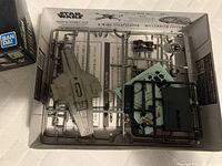 Plastic model kit sprues and parts of the Razor Crest ship unassembled inside the box.