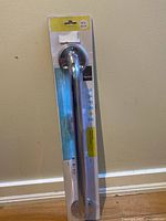 Full view of Taymor Safety grab bar in sealed original plastic packaging against beige wall and baseboard.