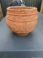 Front and side view of round terracotta pot showing embossed flower patterns and scalloped rim