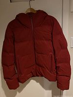 Front view of the burgundy puffer jacket with hood showing zippered pockets and full zipper closure.