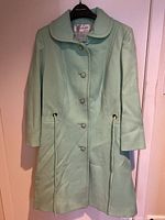 Full view of the mint green wool coat showing front, buttons, collar, and drawstring waist.