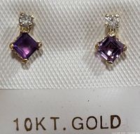 Close-up photo of two 10KT gold earrings with square amethyst stones and round diamonds, displayed on a textured white card stamped '10KT. GOLD'.