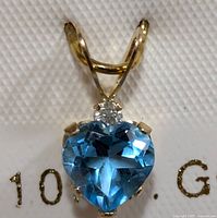 Close-up front view of the pendant showing the blue topaz gemstone and diamond on a white display card.