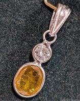 Close-up image of the 14KT gold pendant showing the round diamond above the oval yellow gemstone.