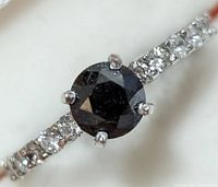 Close-up photo of a 14KT gold ring featuring a round black diamond center stone with smaller clear stones set into the band.