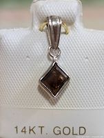 Front view of the diamond pendant showing dark rhombus-shaped diamond in bezel setting and polished gold bail