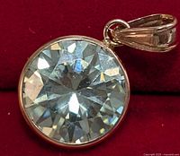 Close-up front view of the round brilliant-cut moissanite stone with rose gold bezel setting against red background