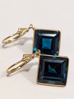 Front view of blue topaz earrings showing deep blue faceted stones in gold bezels with lever-back hooks