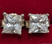 Close-up photo of two stud earrings each with large square-cut clear gemstones mounted in four-prong settings on silver-colored metal.