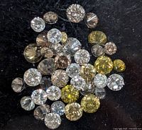 Close-up view of assorted round cut diamonds in white, yellow, and brown colors on black background.