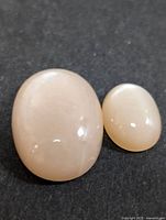 Two polished oval moonstone cabochons resting on a black background, showing their smooth, glossy surfaces and milky white color.