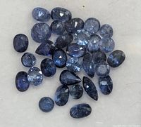 Close-up image of multiple loose faceted sapphires showing different cuts and medium to dark blue colors on a light background.