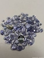 Group of loose genuine tanzanite gemstones in various cuts and sizes, light to medium violet-blue color, with one greenish stone